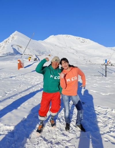Couple portant des sweats N’CO vert et abricot dans la neige