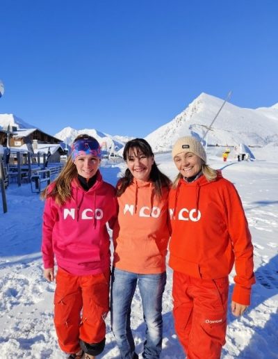 Trois femmes portant des sweats N’CO rose, abricot et rouge à la neige