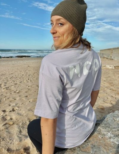 Femme assise sur le sable portant un t-shirt gris N’CO sur la plage